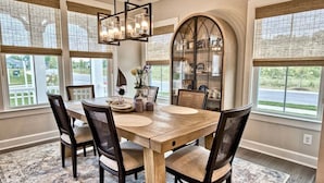 A dining area with a wooden table, chairs, a chandelier, and a view of the outdoors.