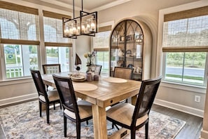 Uma área de refeições com mesa de madeira, cadeiras, um candelabro e vista para o exterior.
