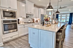 A modern kitchen with white cabinetry, stainless steel appliances, and a large island with seating.