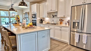 A modern kitchen with white cabinetry, stainless steel appliances, and a large island with seating.