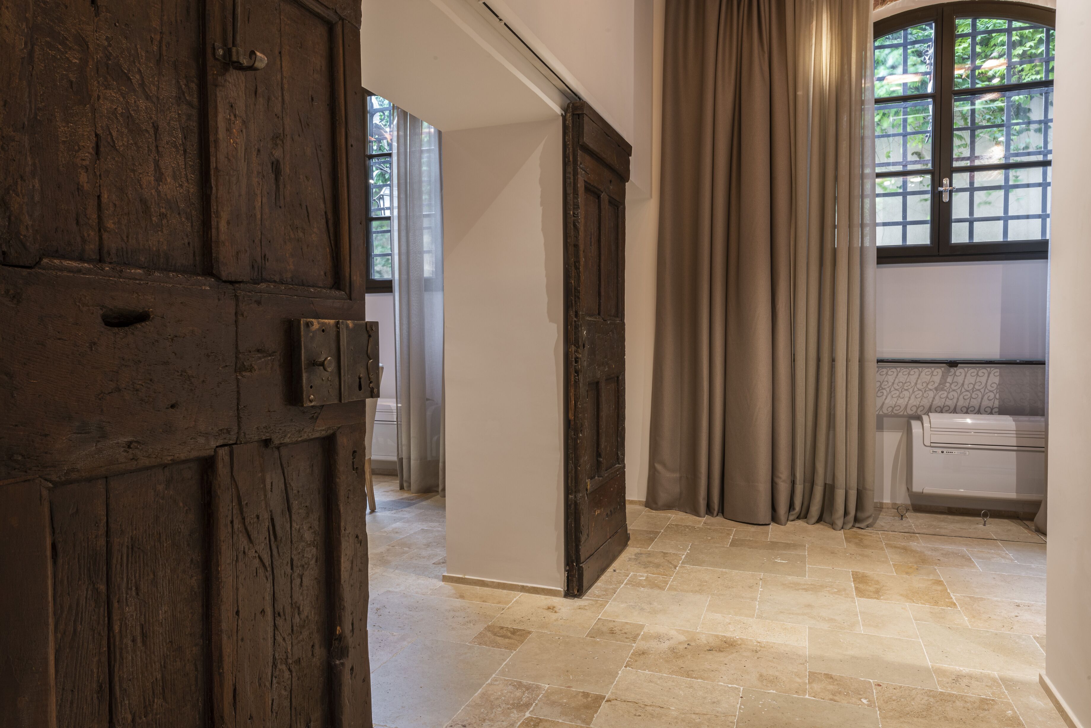 A hallway with a wooden door, a window with curtains, and a tiled floor.