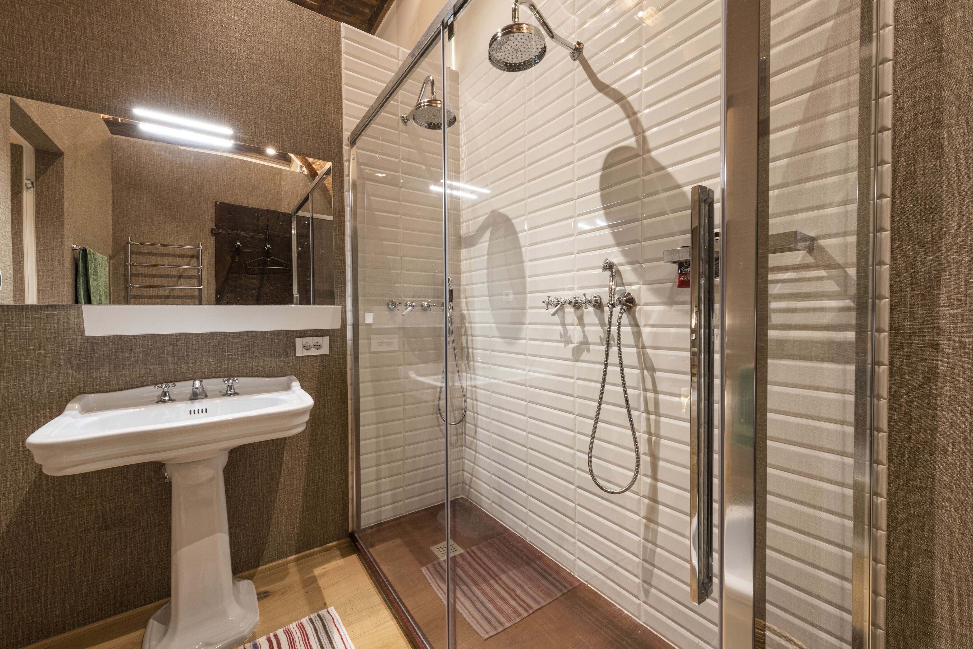 Un bagno moderno con doccia vetrata, lavabo su piedistallo e un grande specchio.