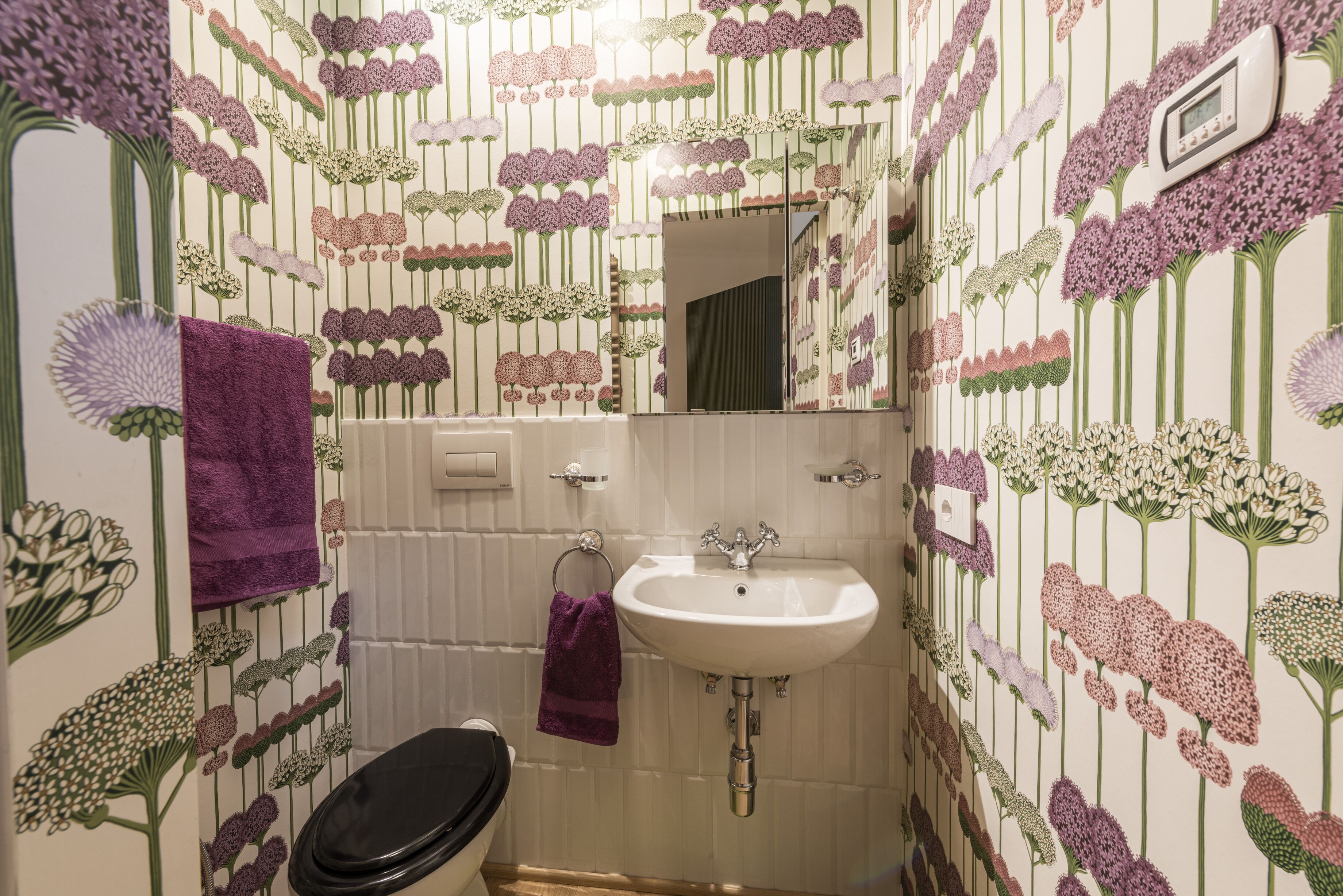 A bathroom with a white sink, a mirror, and a toilet. The walls are decorated with floral wallpaper.