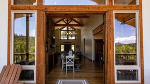 Fachada de madera con ventanas amplias, un comedor con mesa y sillas, y vistas al exterior.