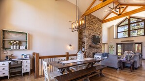 Un amplio espacio de sala con chimenea de piedra, vigas de madera, una mesa de comedor y una acogedora zona de estar.
