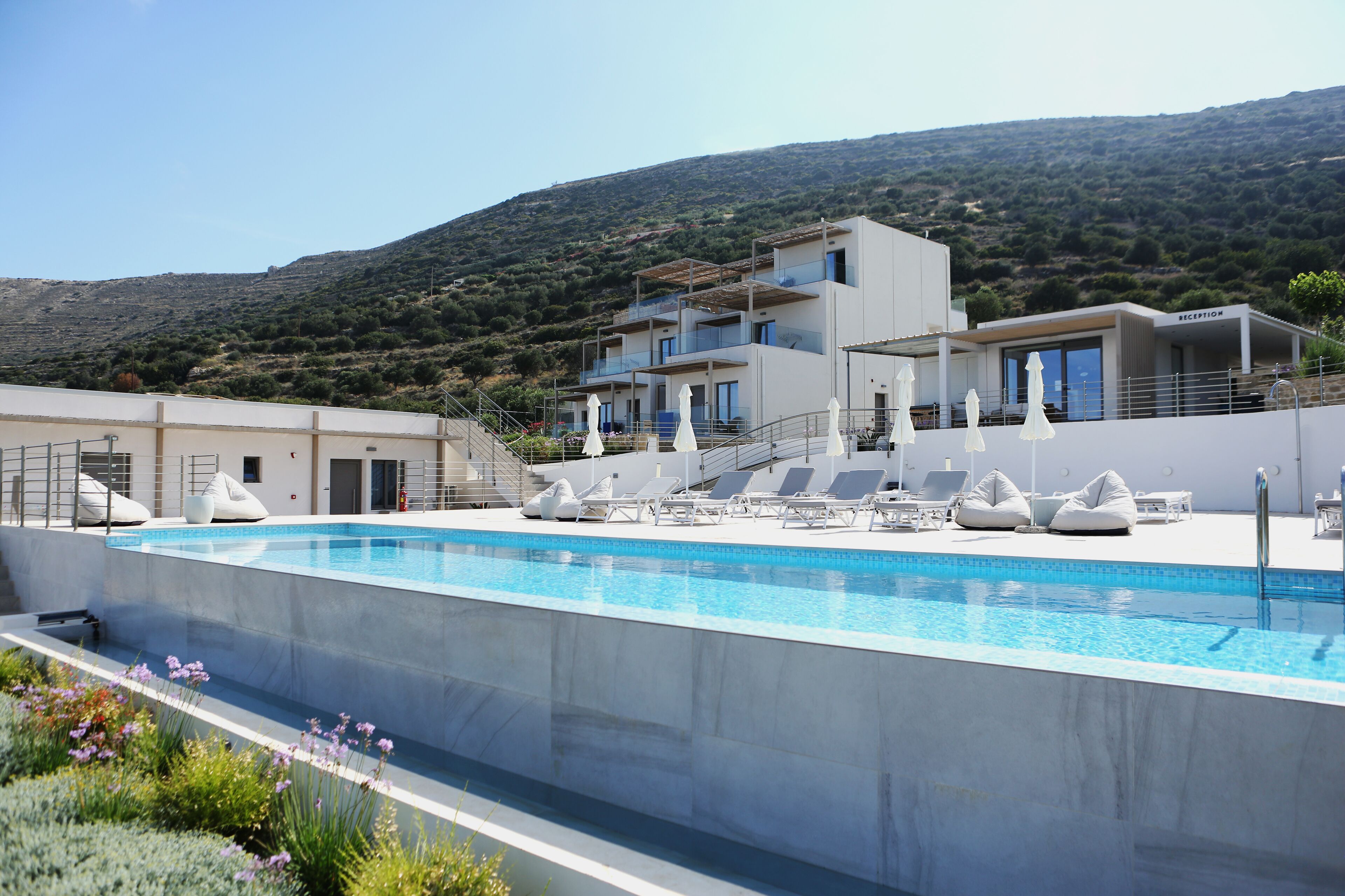 Un hotel moderno con piscina, sillones de descanso y una zona de recepción.