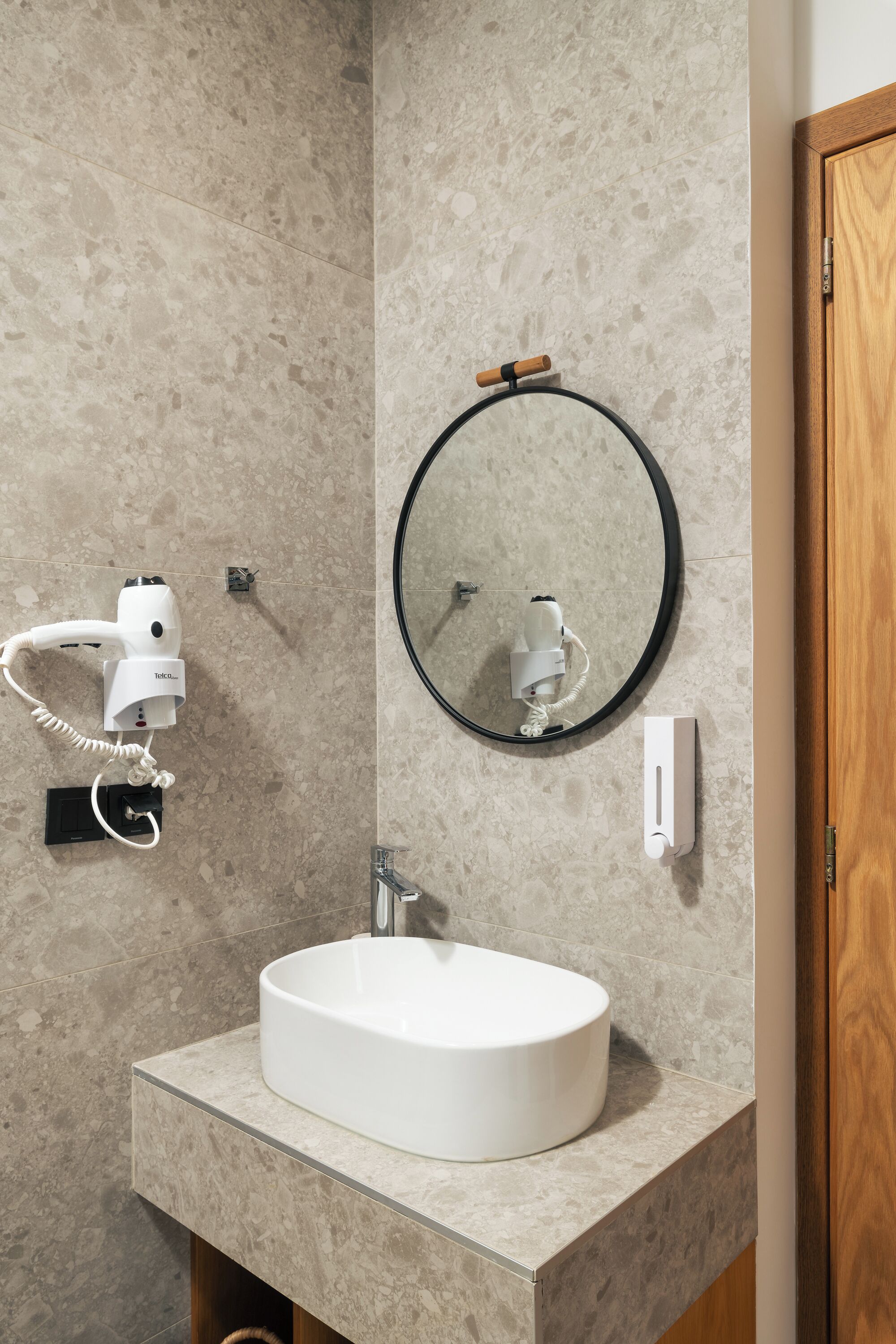 Un bagno con lavandino bianco, uno specchio rotondo, un asciugacapelli e un dispenser di asciugamani.