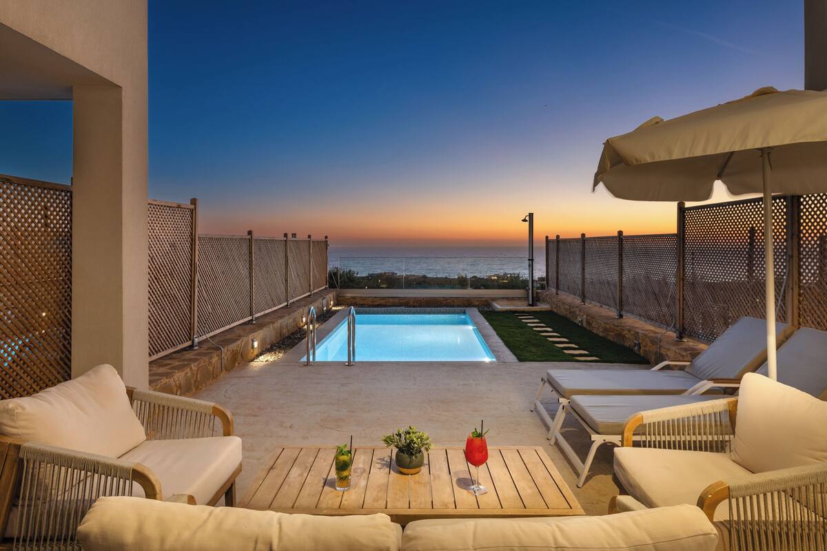 Ein Poolbereich auf dem Dach mit Liegestühlen, einem Tisch und Blick auf den Sonnenuntergang über dem Meer.