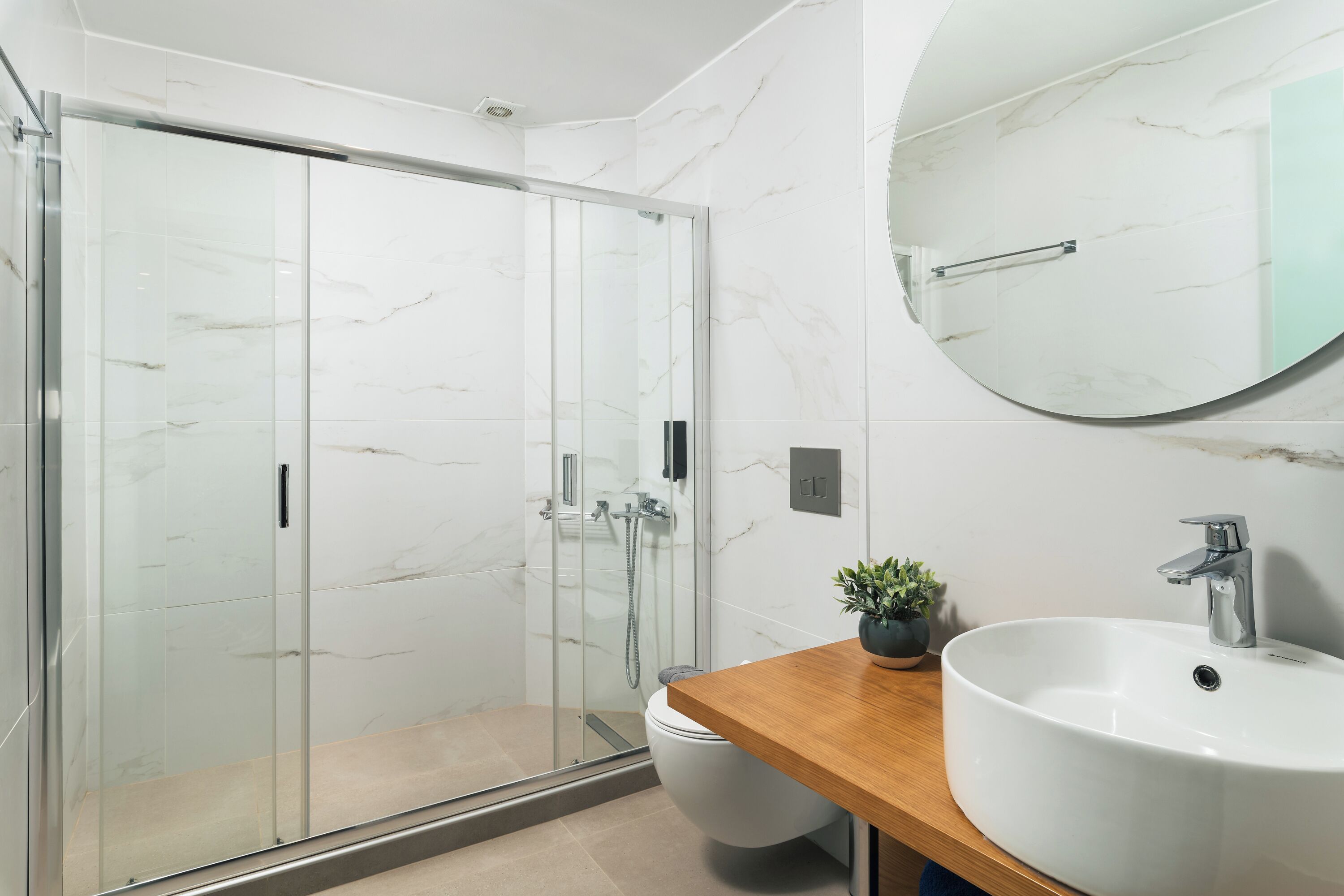 A modern bathroom with a glass-enclosed shower, a wooden vanity, and a large mirror.