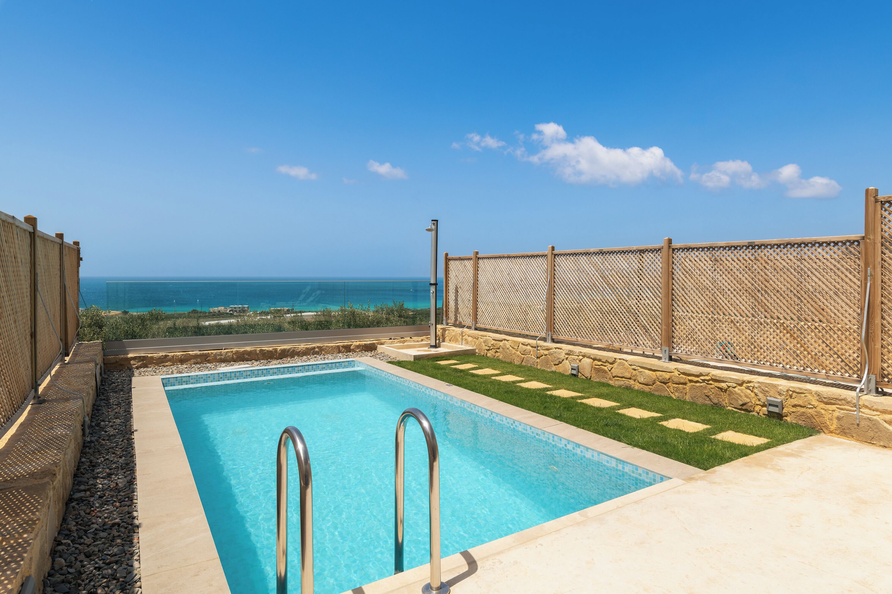 Una piscina con vista al océano, rodeada por una cerca y un muro de piedra.