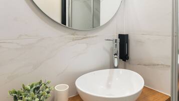 A bathroom with a round mirror, a white sink, a wooden countertop, a potted plant, and a white cup.