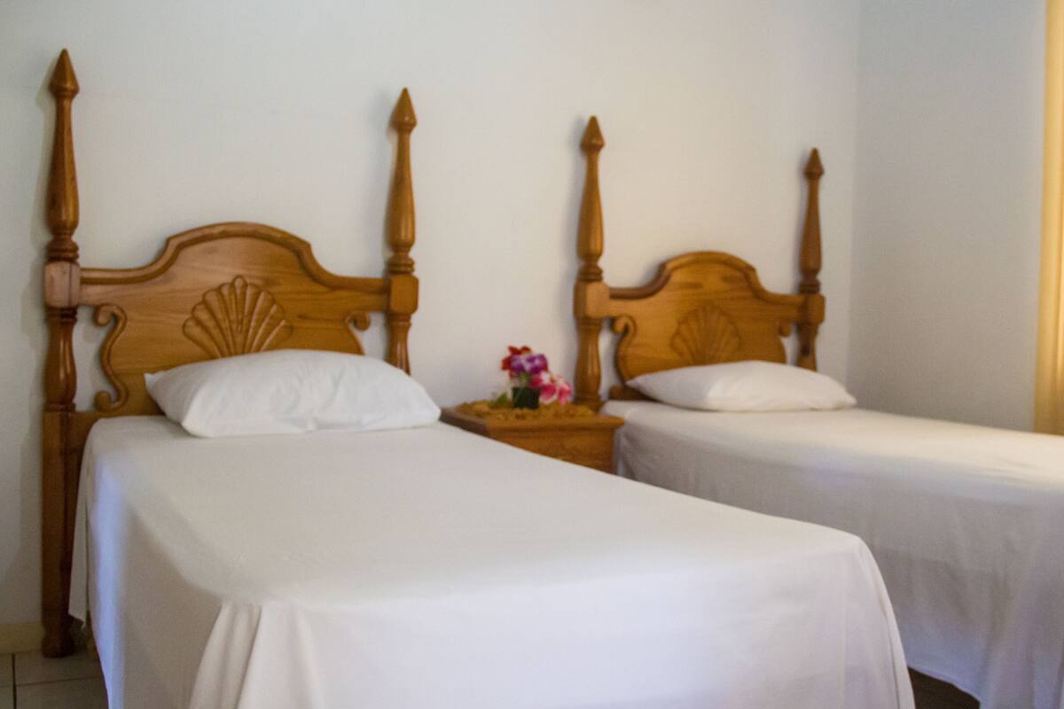 Dos camas individuales con cabeceras de madera, ropa de cama blanca y una mesita de noche con un florero entre ellas.