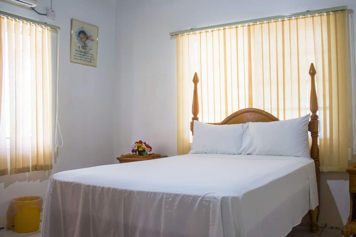 Una cama bien hecha con sábanas blancas, un cabecero de madera y una mesita de noche con un arreglo floral.