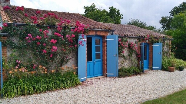 A rustic building with blue doors, surrounded by a gravel driveway and flowering plants. - Calme en Vendée Près de Tout, Idéales Vacances ! (La Garnache)