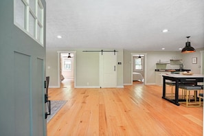 A spacious living area with hardwood floors, a dining table, and a kitchen area with a hanging light fixture.