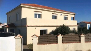 A two-story building with a tiled roof, a small balcony, and a gated entrance. - Appartement 8/10 Personnes Face à la mer (Barbâtre)