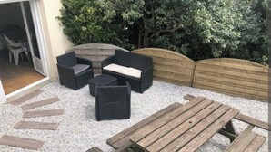 An outdoor seating area with a wooden table and chairs, surrounded by gravel. - Appartement 8/10 Personnes Face à la mer (Barbâtre)