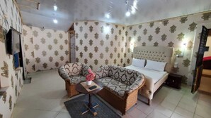 A room with a sofa, a chair, a bed, and a small table with a vase and remote control.