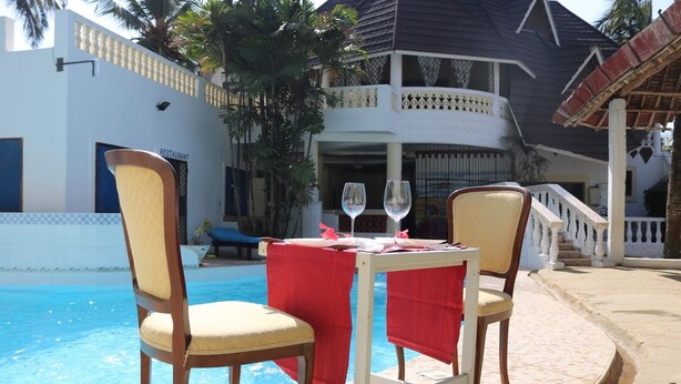A poolside dining area with two chairs and a table, a red tablecloth, and two wine glasses.