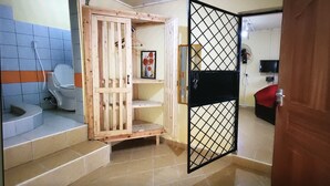 A bathroom with a toilet, a wooden cabinet, a shelf with a picture, and a black metal gate.