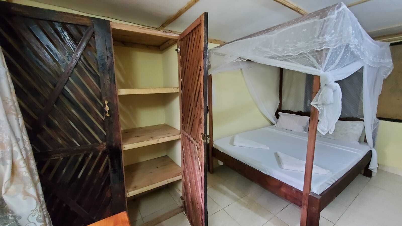 Een eenpersoonsbed met hemelbed, een houten kledingkast en een deur met een geometrisch patroon.