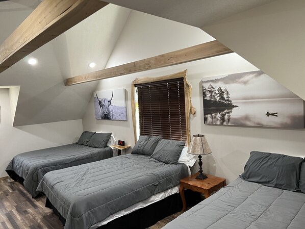 Un dormitorio con dos camas, techo de madera, una mesita de noche con lámpara y dos obras de arte en la pared.