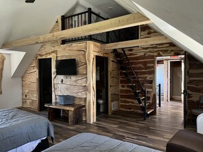 Un dormitorio estilo loft con techo inclinado de madera, un televisor montado en la pared y una escalera que lleva a un nivel superior.