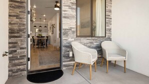 A modern entrance with a stone facade, a glass door leading to a dining area, and two wicker chairs outside. - Putter's Paradise at Desert Color #99 by RedAwning (St. George)