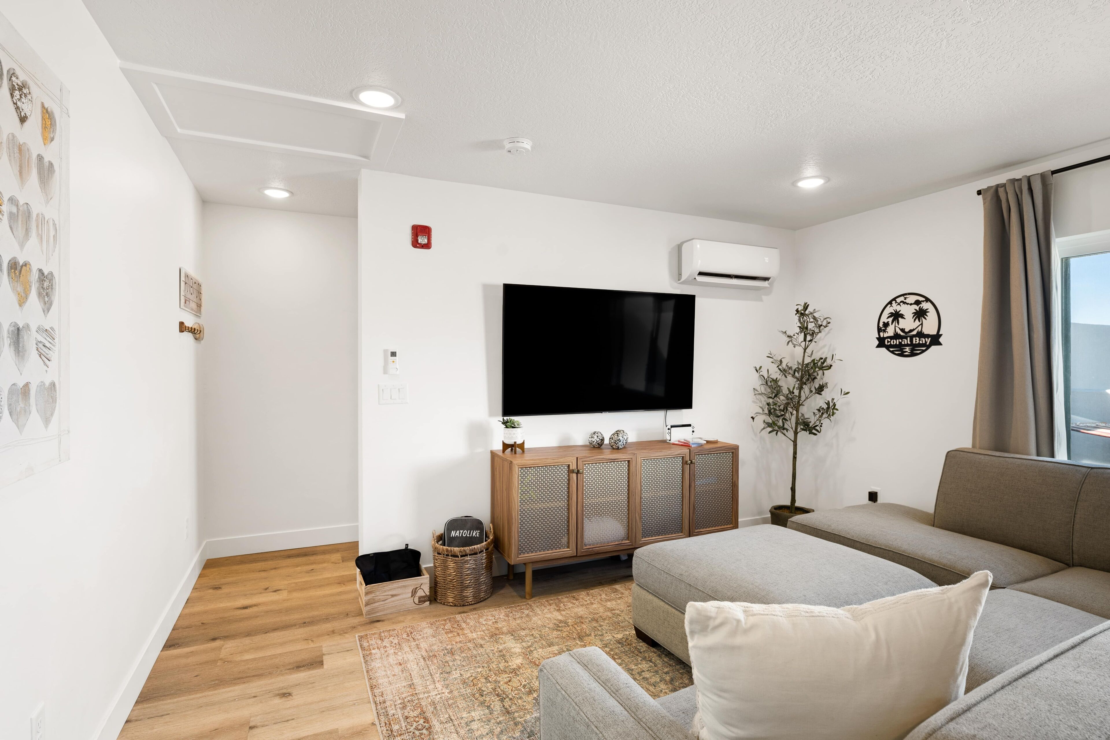 A modern living room with a grey sofa, wooden cabinet, and a flat-screen TV.