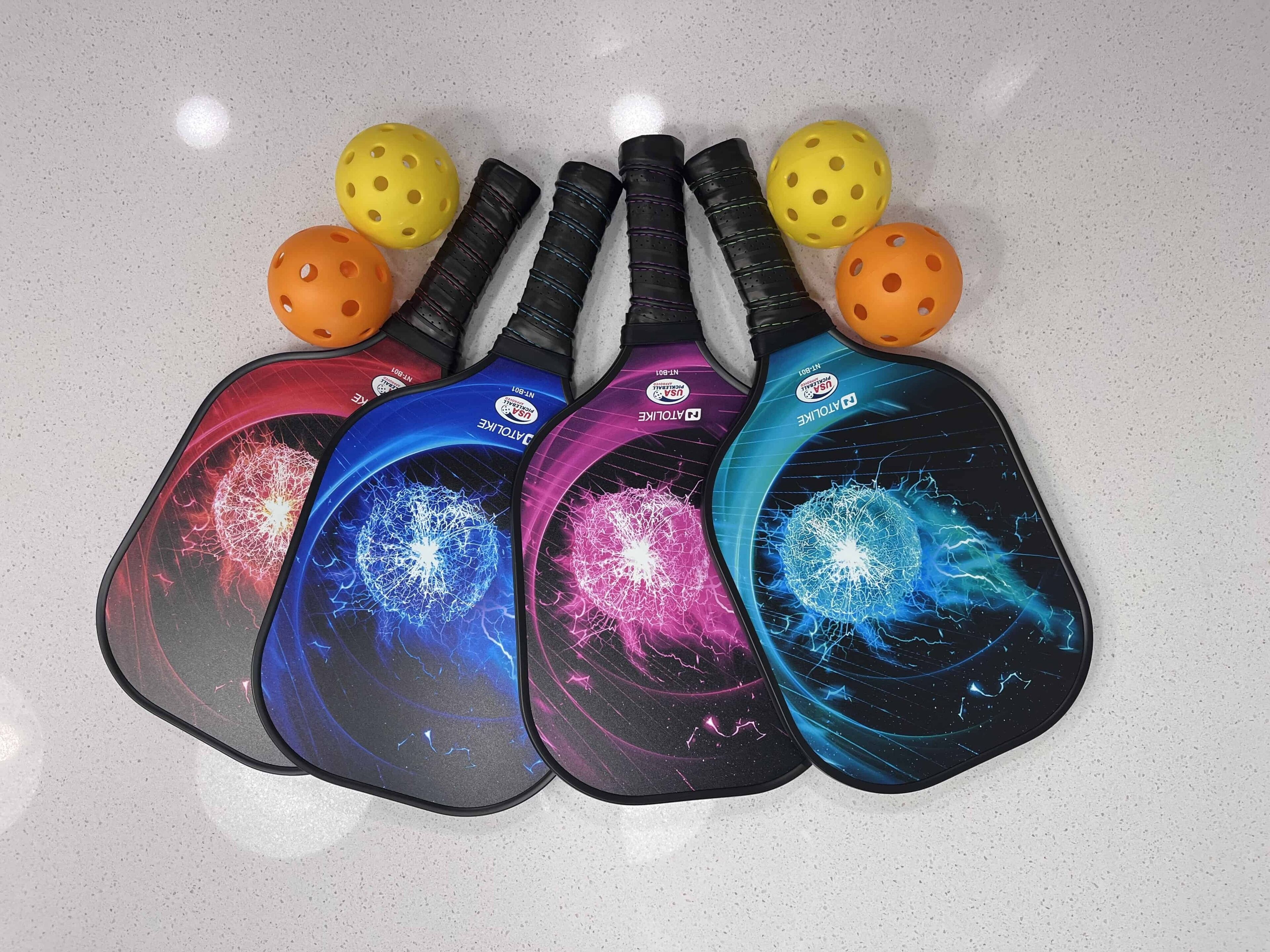 Vijf tafeltennisbats met kleurrijke designs en twee gele tafeltennisballen op een gespikkelde ondergrond.