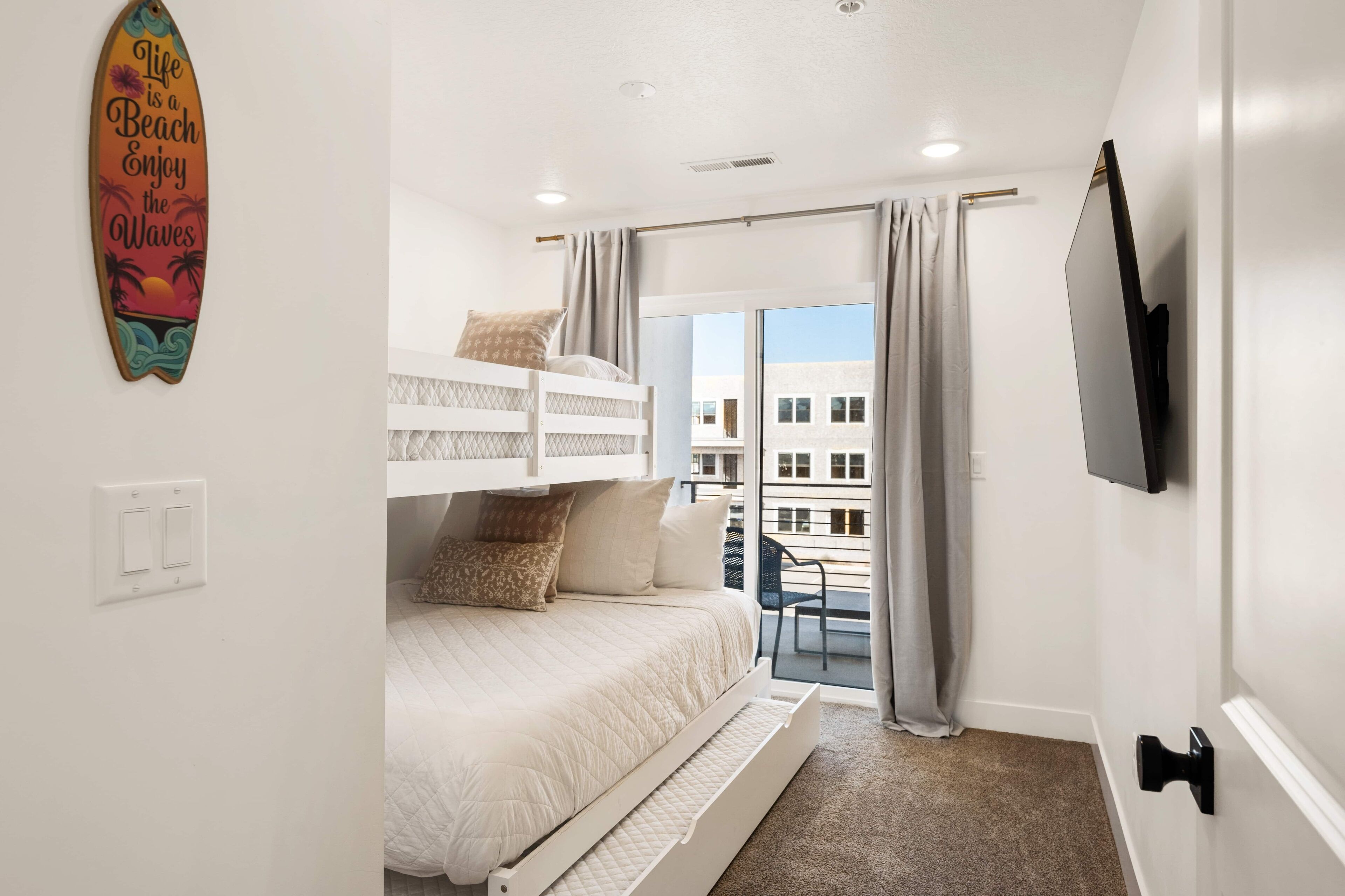 Et soveværelse med køjeseng, skydedør til en balkon og et TV ophængt på væggen.