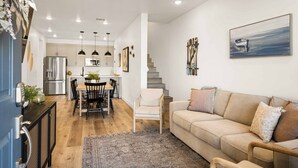 A modern kitchen with stainless steel appliances, a dining area with a wooden table and chairs, and a living area with a beige sofa and a staircase leading to an upper floor. - Putter's Paradise at Desert Color #99 by RedAwning (St. George)