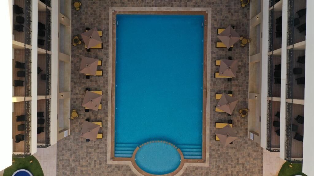 Una piscina en la azotea con sillones de descanso y sombrillas alrededor, todo rodeado por una terraza con baldosas de piedra.