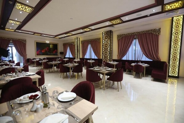 A spacious dining area with multiple tables and chairs, large windows with curtains, and decorative wall panels.