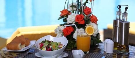 Una mesa de comedor con ensalada, pan, un vaso de jugo de naranja, un arreglo floral y saleros y pimenteros.
