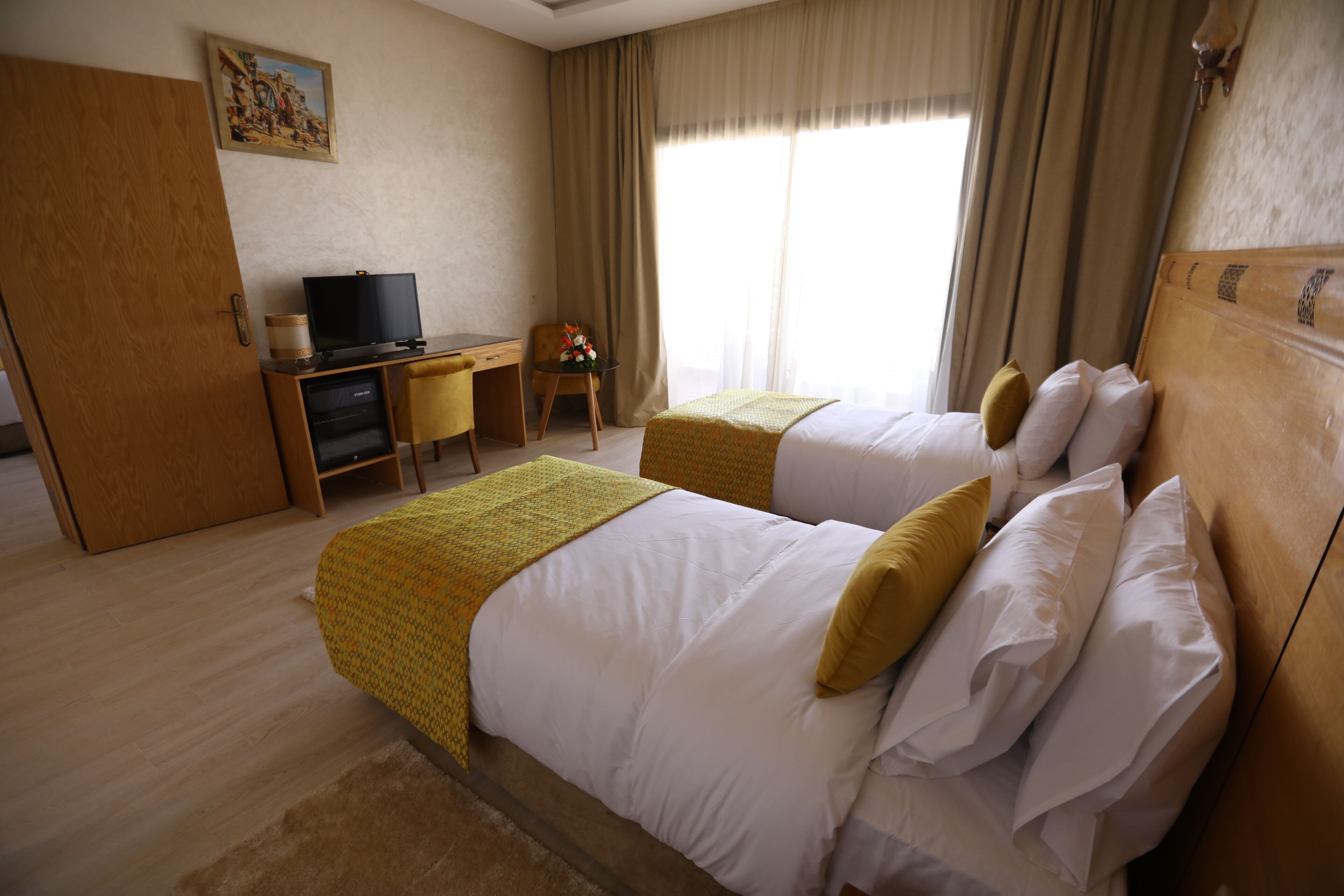 Une chambre d’hôtel avec deux lits, un bureau avec une télévision et une fenêtre avec des rideaux.