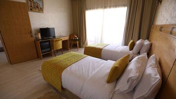 Una habitación de hotel con dos camas, un escritorio con televisor y una ventana con cortinas.