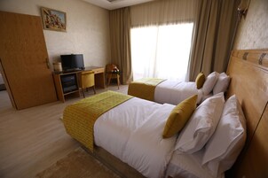 Una habitación de hotel con dos camas, un escritorio con televisor y una ventana con cortinas.