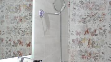 A bathroom with a sink, mirror, shower, and floral wallpaper.