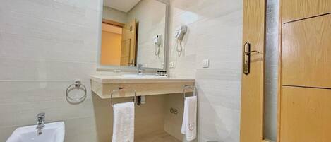 A modern bathroom with a wooden vanity, a bidet, a mirror, and a small trash bin.