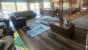 Uma sala de estar espaçosa com um sofá grande, uma mesa de centro e um tapete. Há também uma cozinha com armários de madeira e uma mesa de jantar.