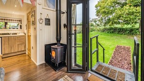 A modern kitchen with wooden cabinets, a stove, and a view of a green garden through an open door. - Two-Level Shepherd`s Hut · Sleeps 4 with Kids` Den · Fire Pit near Dartmouth (Dartmouth)
