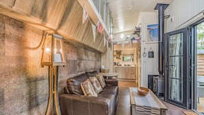 A cozy living room with a leather sofa, a wooden coffee table, and a rustic wall. - Two-Level Shepherd`s Hut · Sleeps 4 with Kids` Den · Fire Pit near Dartmouth (Dartmouth)
