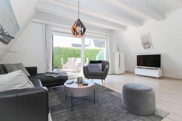 Een moderne woonkamer met een bank, fauteuil, poef en een tv-meubel.