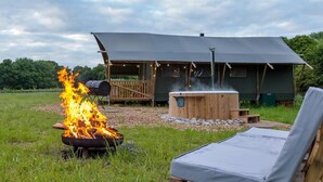 A rustic outdoor setting with a fire pit, a wooden deck, a hot tub, and a covered structure. - Awe Inspiring two storey tent (Crowhurst)