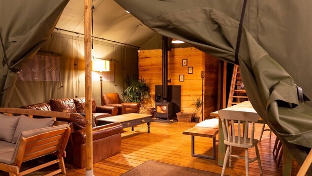 A cozy tented accommodation with a wooden interior, a sofa, a table, and a fireplace. - Awe Inspiring two storey tent (Crowhurst)