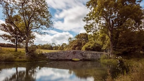 A stone bridge over a calm river, surrounded by trees and grassy fields. - Awe Inspiring two storey tent (Crowhurst)