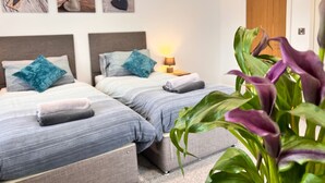 Une chambre d’hôtel avec deux lits, une table de chevet avec une lampe et une grande plante.