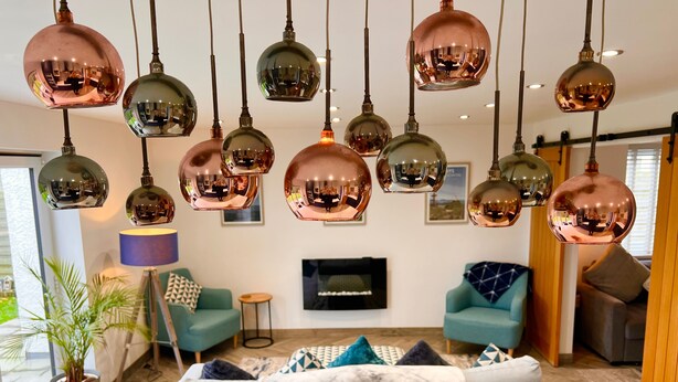 Un salon moderne doté de plusieurs suspensions en cuivre, d’un grand téléviseur à écran plat et d’un coin salon confortable agrémenté d’un plaid en marbre.