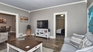 Un salon comprenant un téléviseur, un canapé, une table basse et un coin repas avec des chaises.